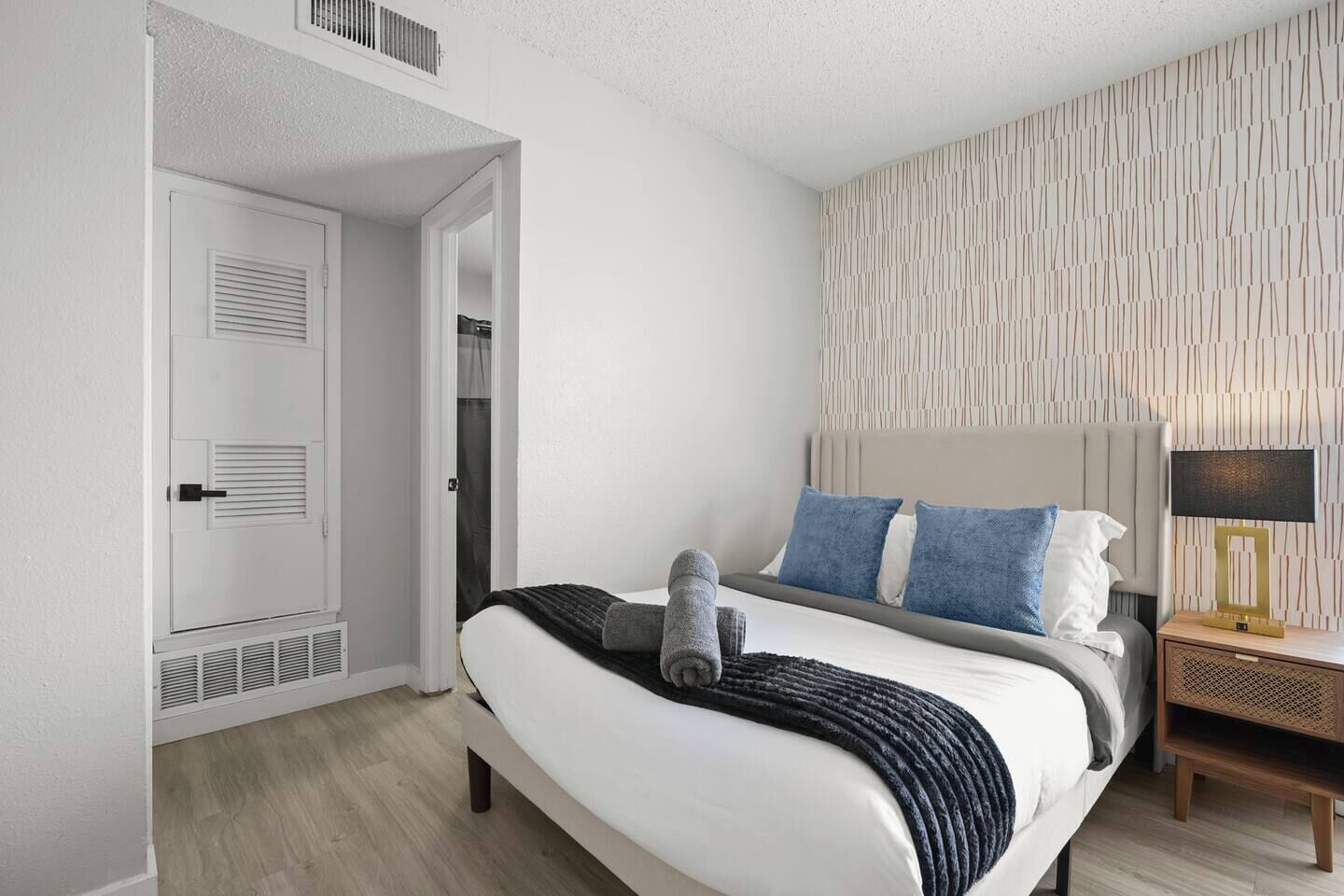 A modern hotel room with a bed, bedside table, and a patterned wall.