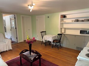 A room with a dining table, chairs, a vase with flowers, a microwave, and a cabinet with dishes. - Charming Cozy 1-bedroom furnished apartment on 12 peaceful acres in Dorset . (Dorset)