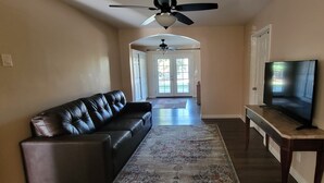 A living room with a leather sofa, a television on a stand, a ceiling fan, and a view into the dining area. - Lovely family-friendly 3-bedroom bungalow in peaceful Santa Paula (Santa Paula)