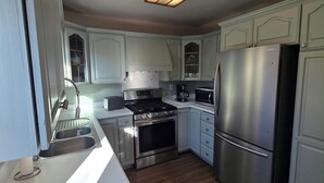 A kitchen with white cabinets, stainless steel appliances, a wooden ceiling light, and a wooden floor. - Lovely family-friendly 3-bedroom bungalow in peaceful Santa Paula (Santa Paula)