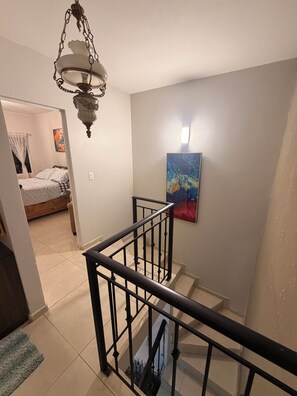Un escalier avec une rampe noire, un tableau au mur et un lustre.