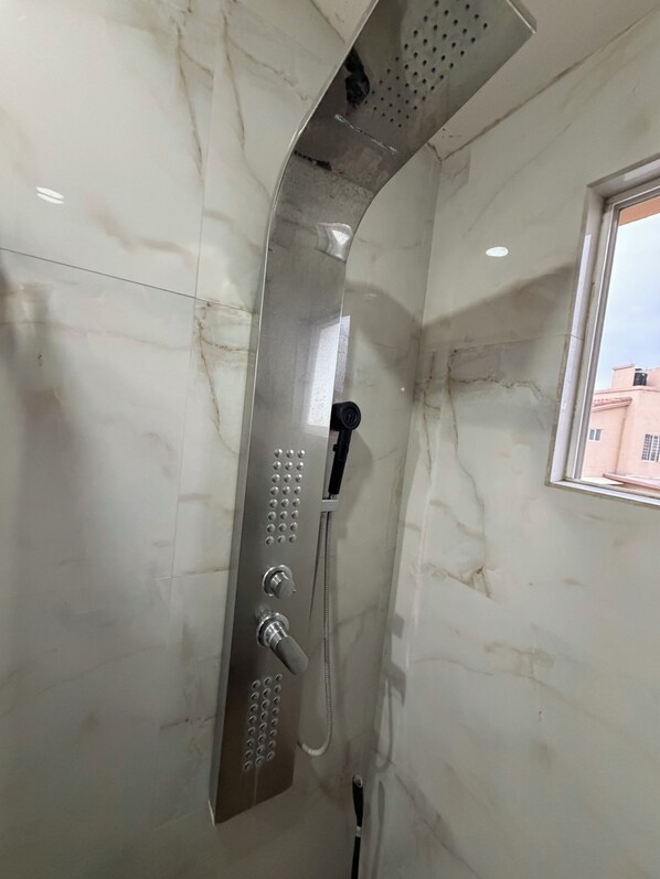 A shower with a handheld showerhead and a wall-mounted control panel.