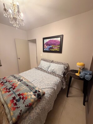 A bedroom with a bed, a bedside table with a lamp, a framed picture on the wall, and a door. - House in the Real Madeira Subdivision (Pachuca de Soto)