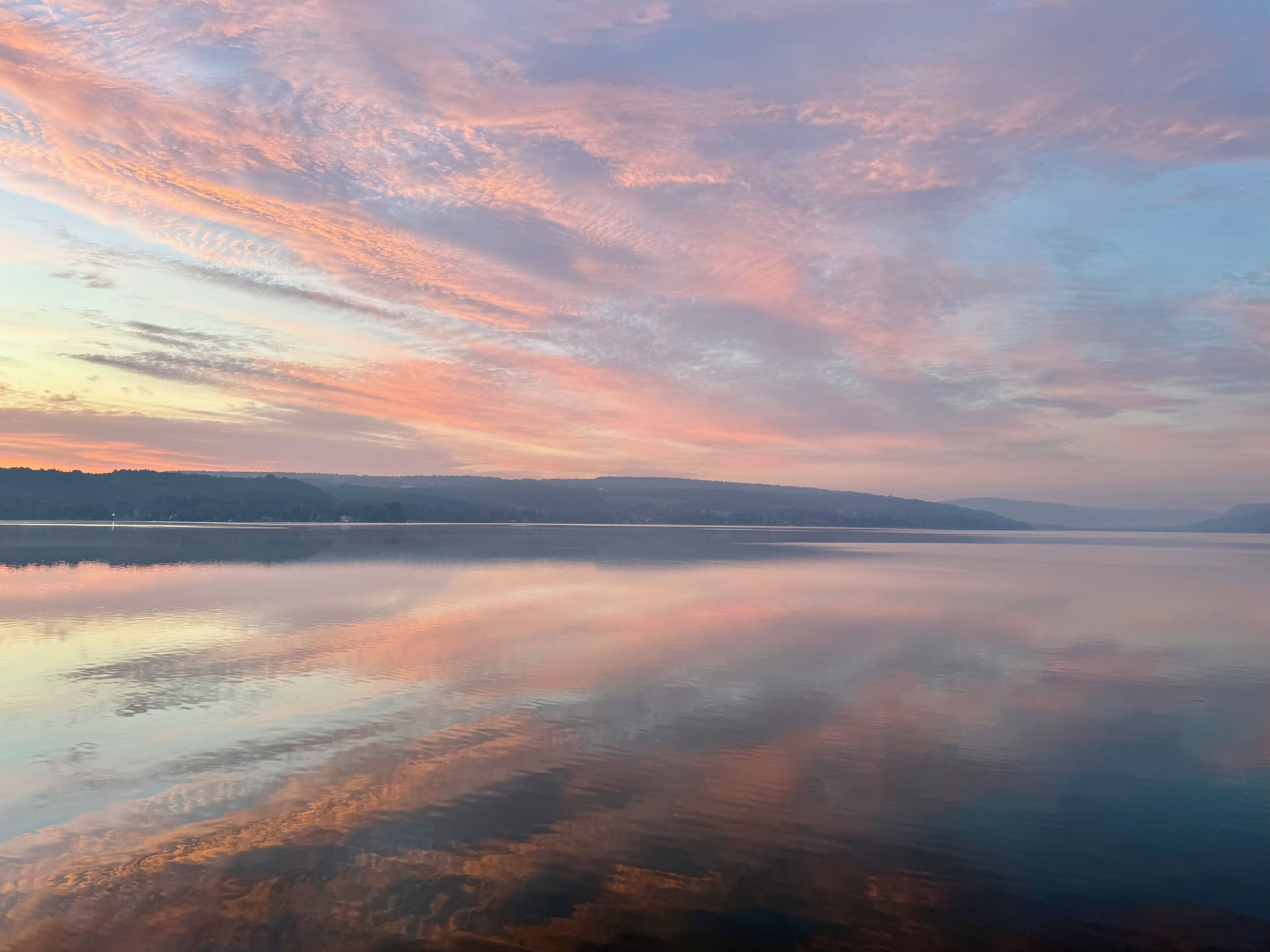 En stilla sjö med en klar spegelbild av himlen, omgiven av ett kuperat landskap.