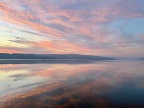 A calm lake with a clear reflection of the sky, surrounded by a hilly landscape. - Beautiful lakehouse on Otisco Lake. Lakeside deck.  Private and serene. (Marietta)