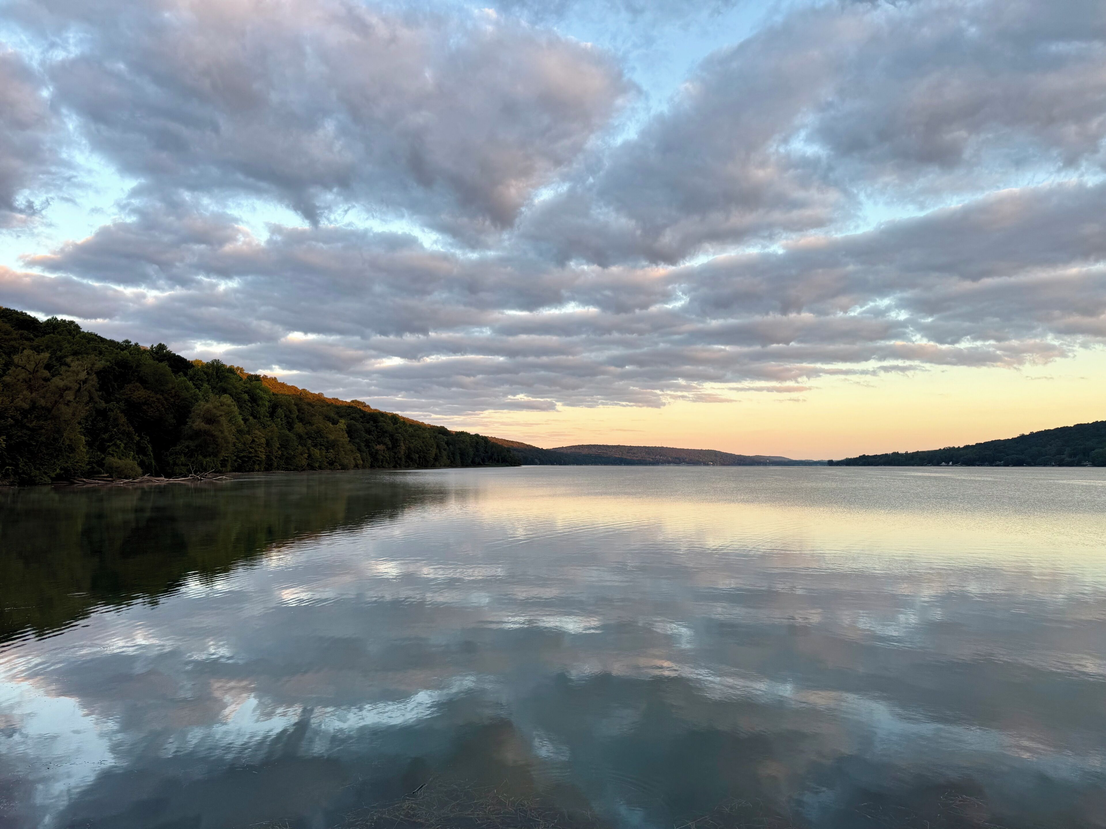 A calm lake with a forested hillside and a cloudy sky.