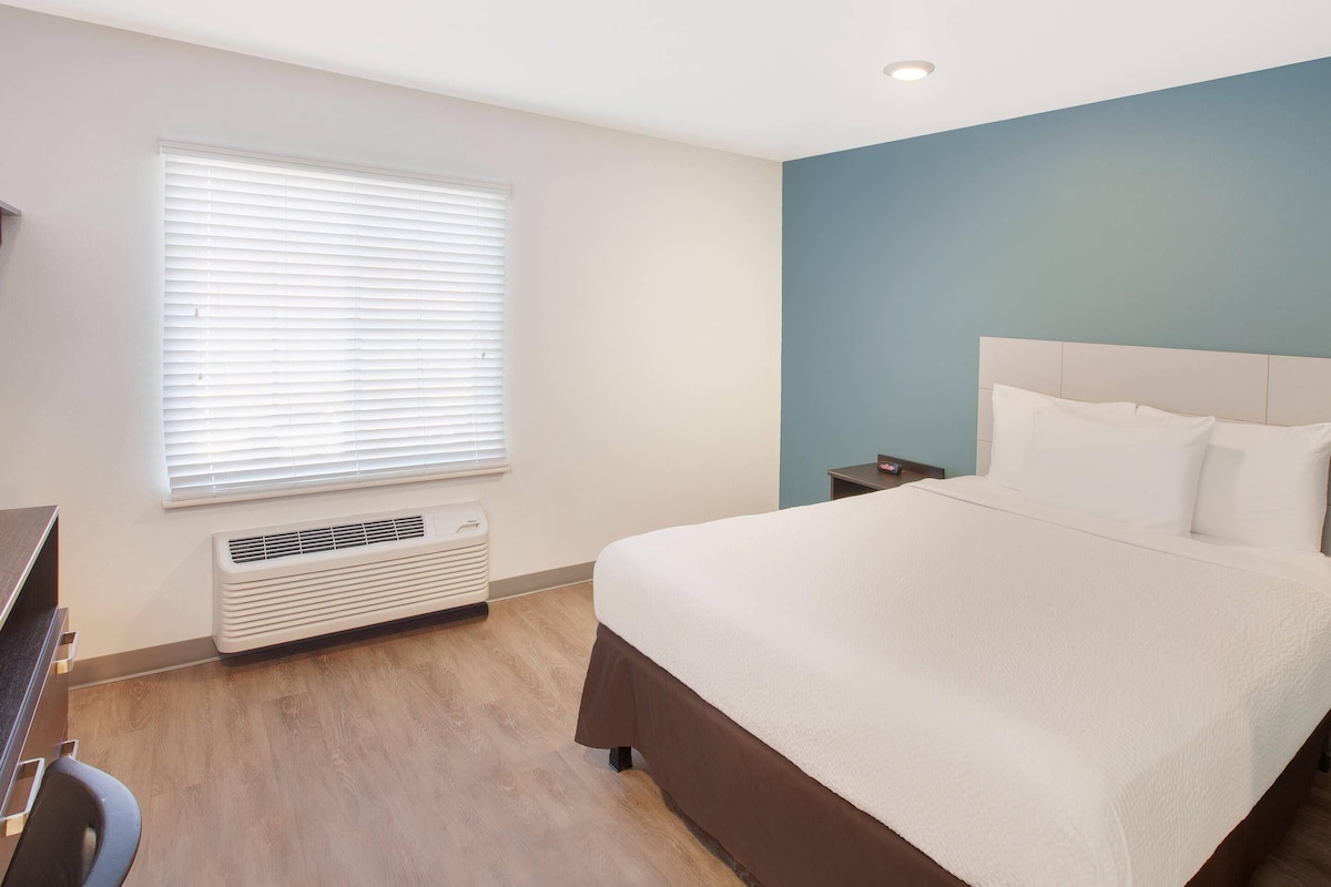 Ein Hotelzimmer mit Bett, Nachttisch und Fenster mit Jalousien.
