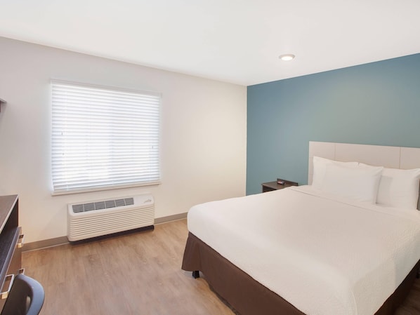 Ein Hotelzimmer mit Bett, Nachttisch und Fenster mit Jalousien.