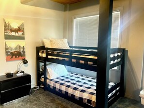A bunk bed with a checkered bedspread, a bedside table with a lamp, and two wall art pieces depicting animals. - Vista Grande-2 Hot Tubs! 3 Large Decks! Arcade! (Ruidoso)