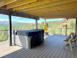 Een terras buiten met een jacuzzi, houten stoelen en uitzicht op een bergachtig landschap.