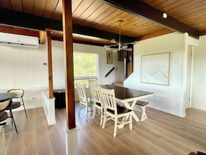 A spacious room with a wooden dining table and chairs, a large window, and a ceiling with exposed beams. - Vista Grande-2 Hot Tubs! 3 Large Decks! Arcade! (Ruidoso)
