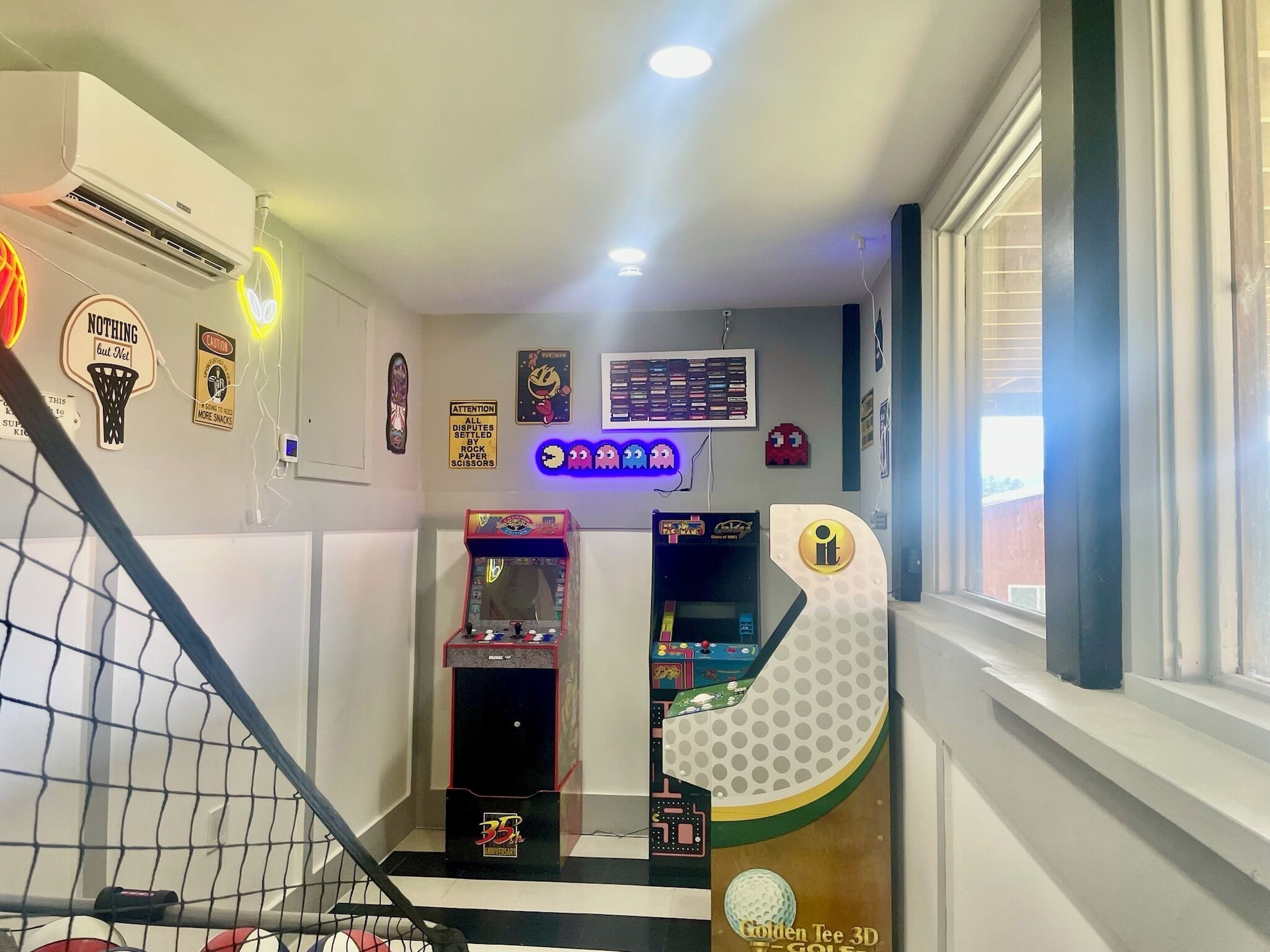 A room with a basketball hoop, arcade games, and a window with blinds.