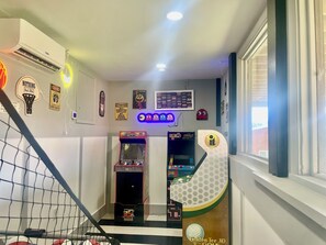 Quarto com cesta de basquete, jogos de fliperama e janela com persianas.