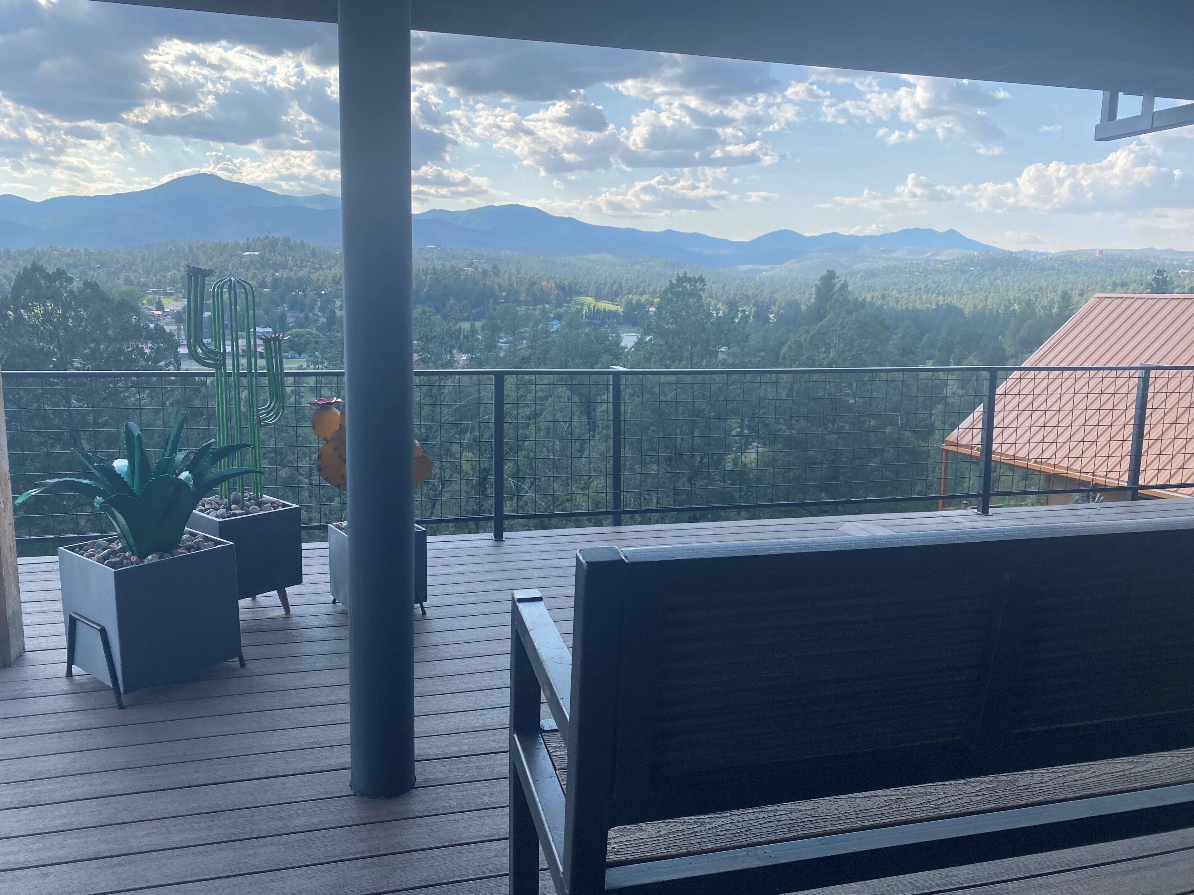 Un balcon doté d’un plancher en bois, d’une rambarde en métal et d’un banc.