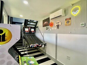Et værelse med basketballkurv, en neonlys-reklame og en ventilator monteret på væggen.