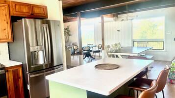 A modern kitchen with stainless steel appliances, a central island, and a dining area with chairs and a table.