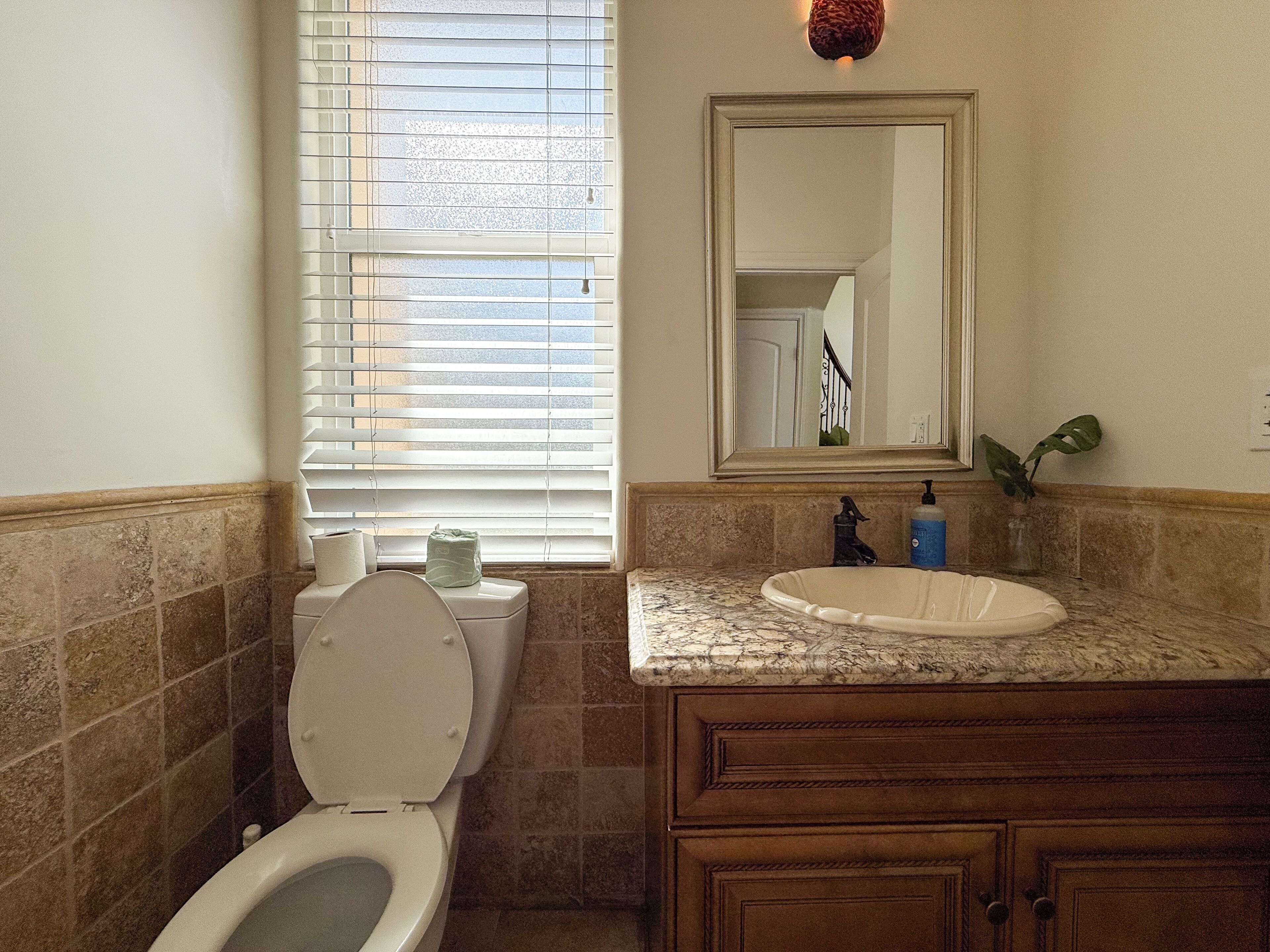 A bathroom with a toilet, sink, mirror, and window with blinds.