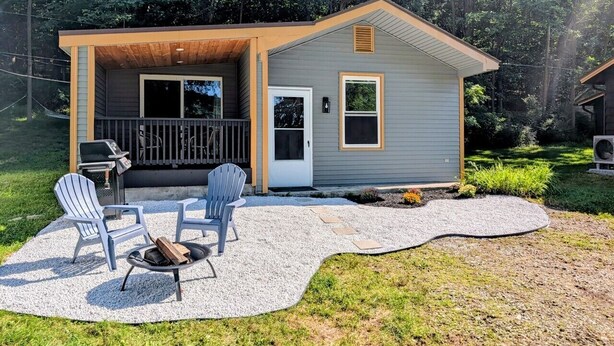 A small house with a covered patio, a grill, and two Adirondack chairs.