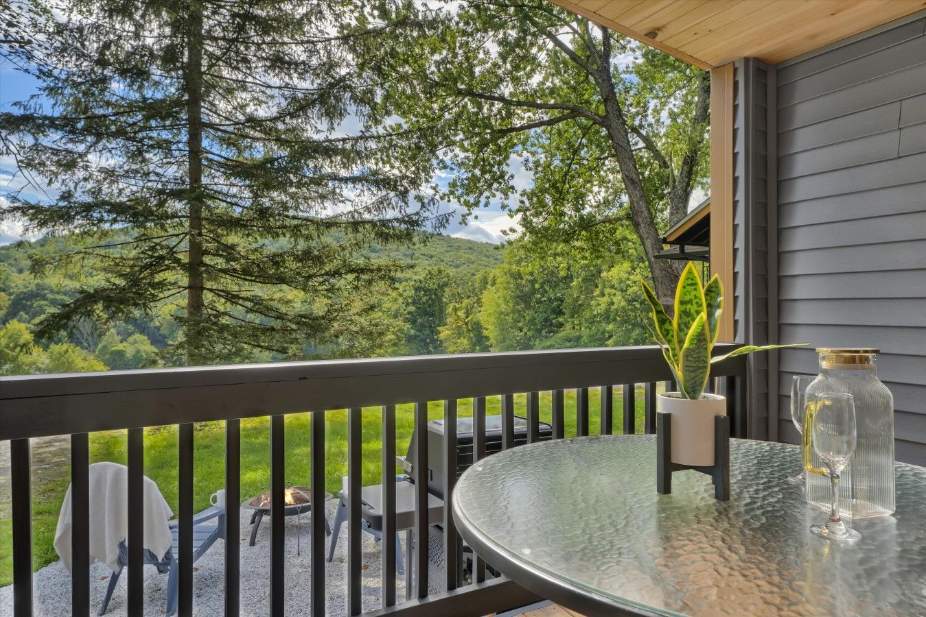 A balcony with a glass table, a potted plant, and a bottle.