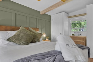 A neatly made bed with pillows, a bedside lamp, and a window with a view of greenery.