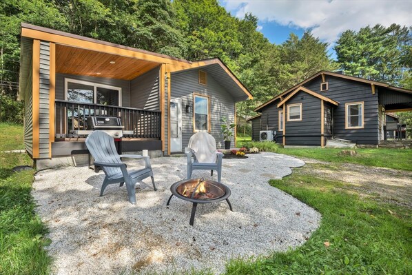 A two-story cabin with a covered patio, outdoor seating, and a fire pit.