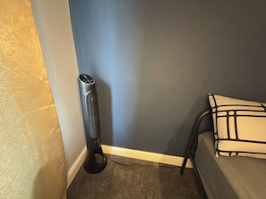 A corner of a room with a standing heater, a bed with a patterned pillow, and a wall with a textured finish. - Room-bright Double Size Private Room in (Wellingborough)