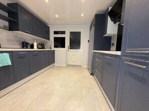 A modern kitchen with dark cabinets, a white countertop, and a tiled floor. - Room-bright Double Size, Private Room in (Wellingborough)