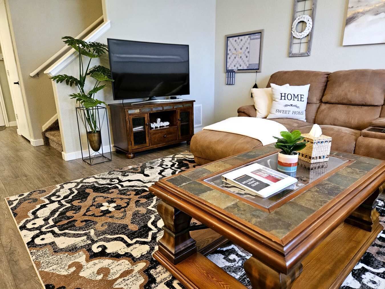 Een woonkamer met een televisie, bank, salontafel en een vloerkleed met een patroon.