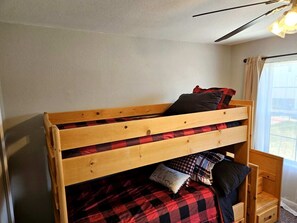 A bunk bed with a wooden frame, a red and black checkered bedspread, and a pillow with text. - Summit Retreat - Furnished Townhome, 2-Car Garage, Colorado Springs (Colorado Springs)