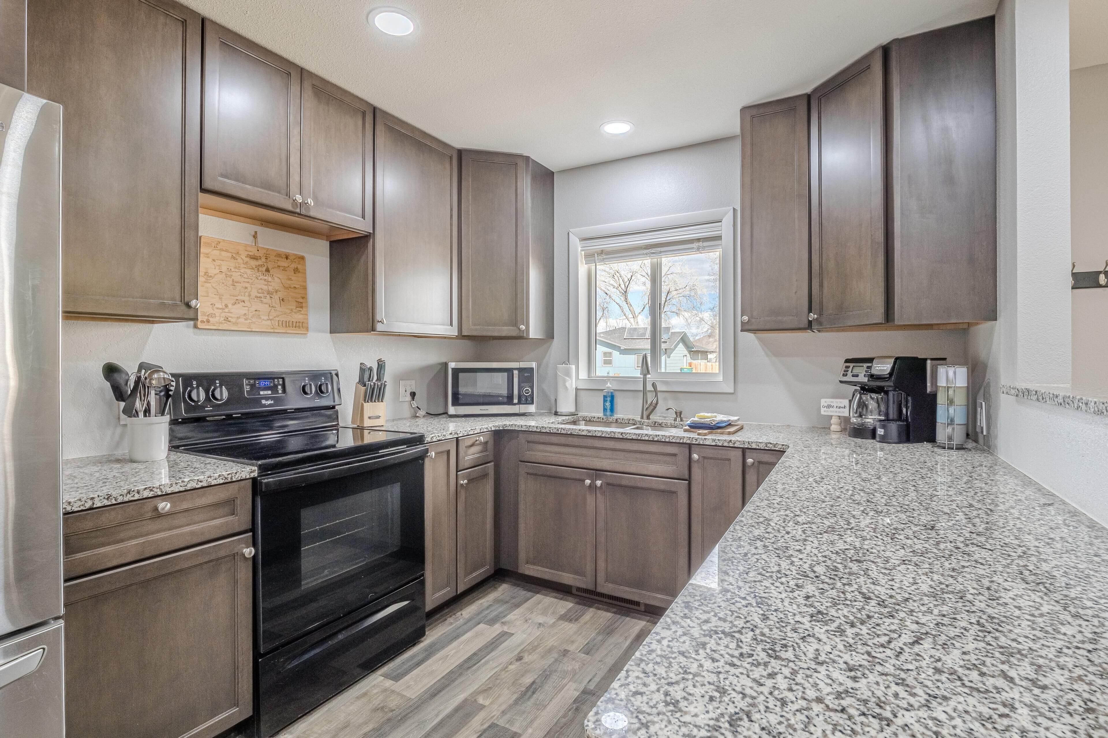 A kitchen with dark wooden cabinets, granite countertops, a stainless steel refrigerator, a built-in oven, a microwave, and a coffee maker.