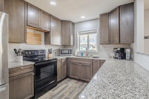 Eine Küche mit dunklen Holzschränken, Granit Arbeitsplatten, einem Edelstahl-Kühlschrank, einem eingebauten Backofen, einer Mikrowelle und einer Kaffeemaschine.