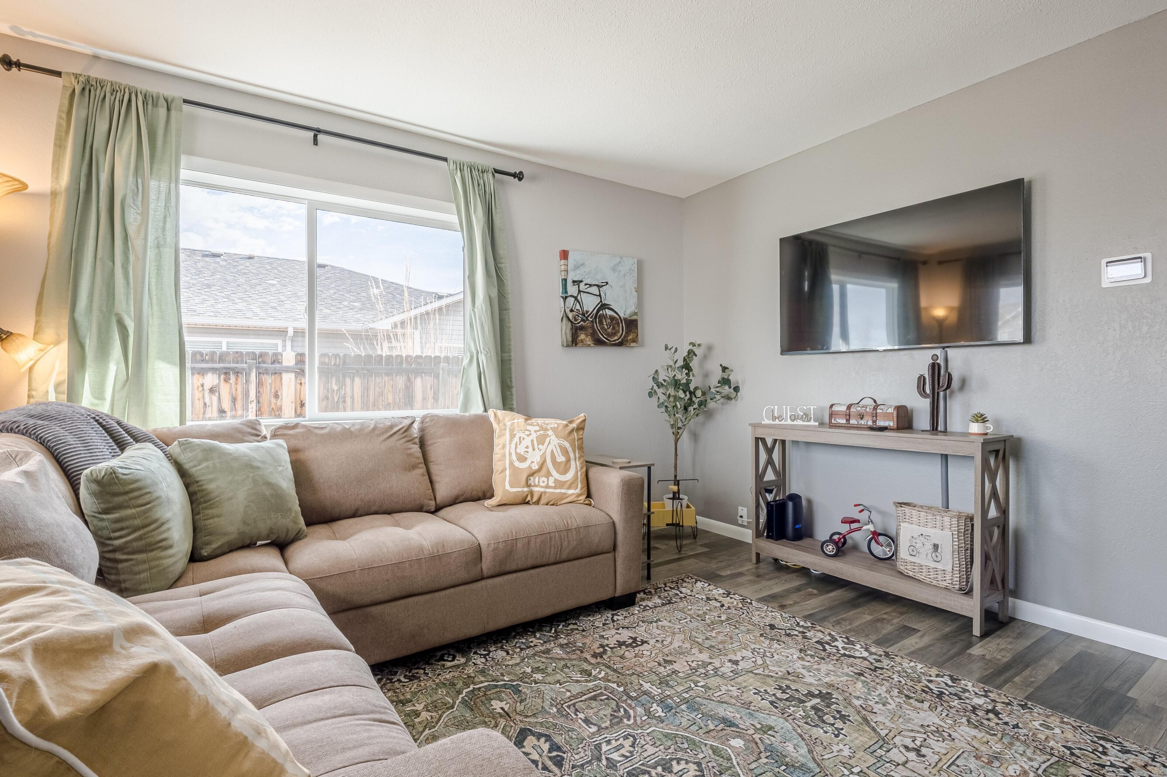Una sala de estar con un sofá color beige, un tapete estampado, un televisor y un mueble de madera con una bicicleta y un triciclo.