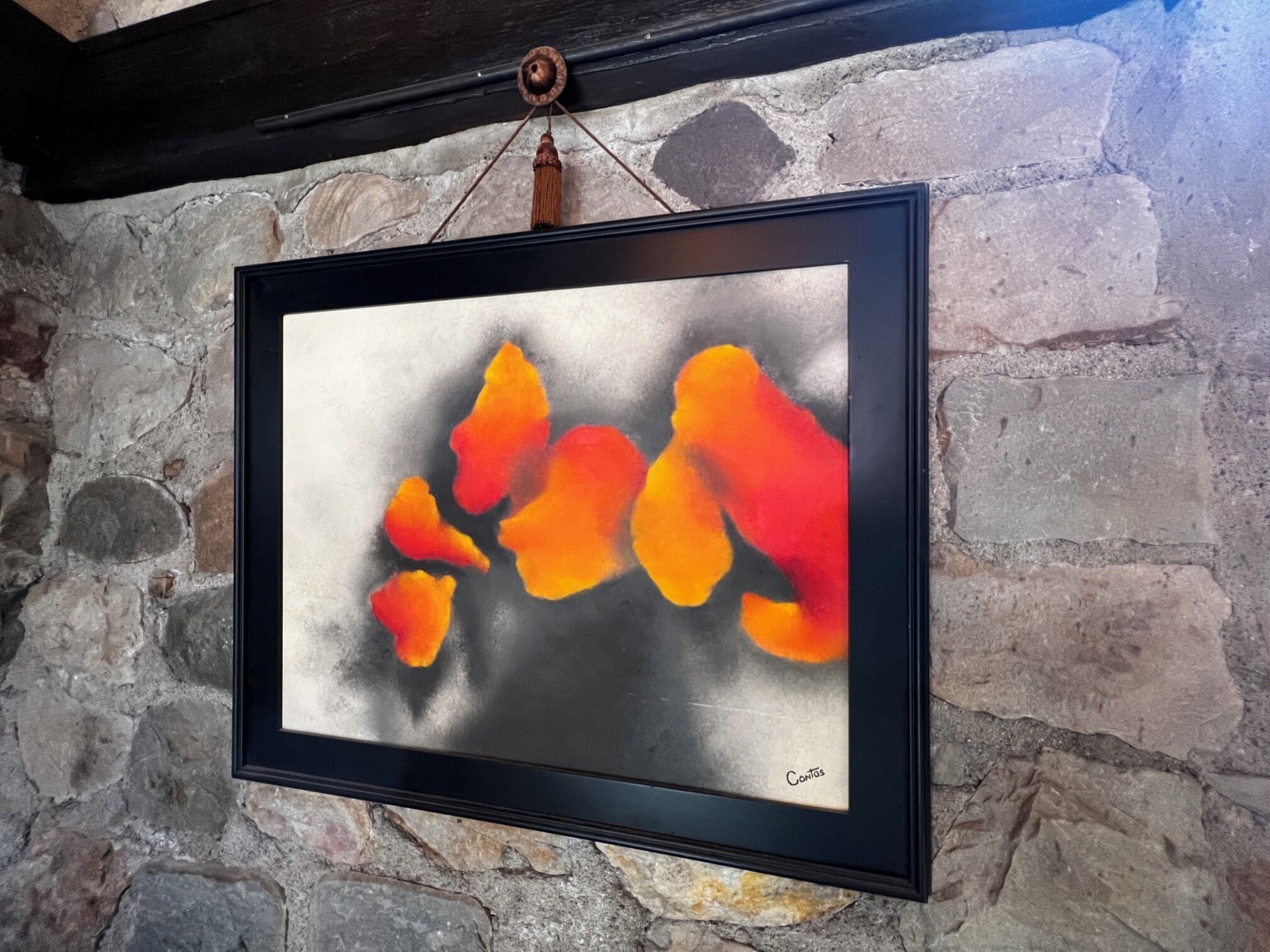 A framed abstract painting with a black frame hanging on a stone wall.