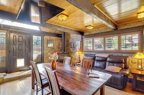 Un interior rústico con una mesa de comedor de madera, sillas, un sofá de cuero y una chimenea de piedra.