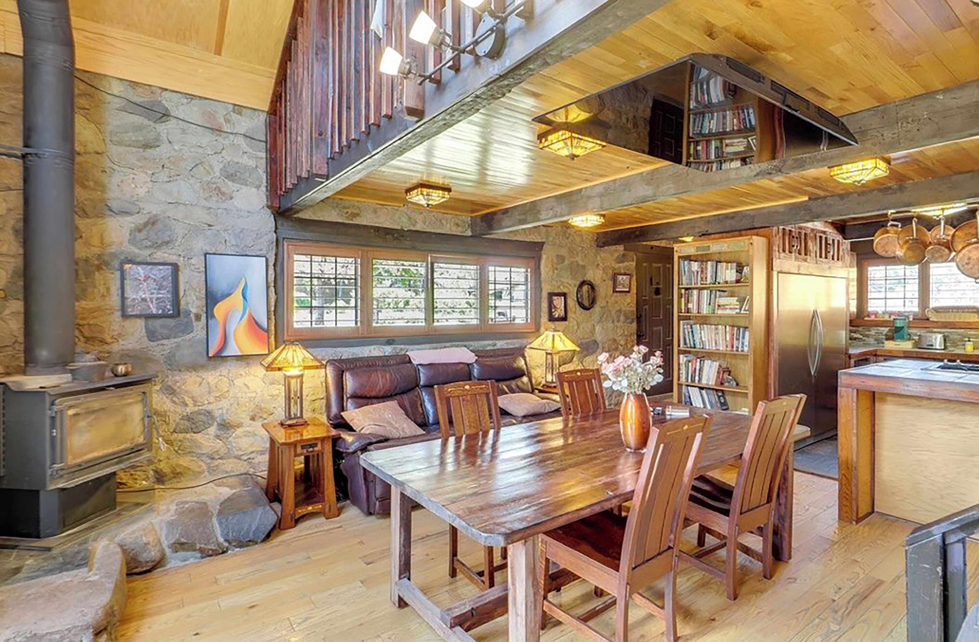 Un interior rústico con pared de piedra, muebles de madera, chimenea y zona de cocina.