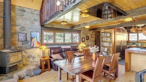 Un interior rústico con pared de piedra, muebles de madera, chimenea y zona de cocina.