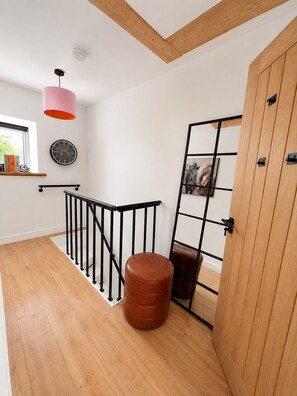 A modern interior with a wooden floor, a staircase with black railings, a red pendant light, and a wooden door. - Mountain Backdrop Miners Cottage with Pizza Oven (Blaenau Ffestiniog)
