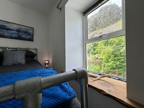A bedroom with a bed, a window with a view of greenery and mountains, and a painting on the wall.