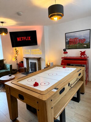Una habitación con mesa de futbolín, televisor mostrando 'NETFLIX' y chimenea.