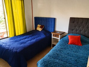 Habitación con dos camas, cada una con un diseño de cabecera diferente, una mesita de noche y una ventana con cortinas.