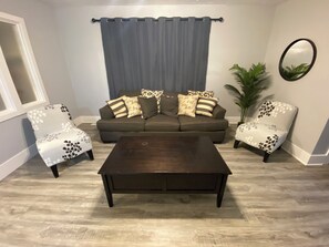 Ein Wohnzimmer mit einer Couch, zwei Sesseln, einem Couchtisch, einer Topfpflanze und einem Spiegel an der Wand.