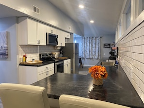 A modern kitchen with white cabinets, a black countertop, and a microwave. There is a dining area with a table and chairs, and a flower vase on the countertop.