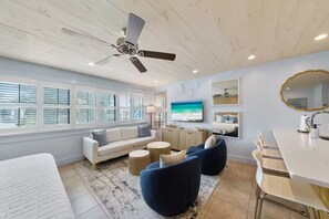 Ein modernes Wohnzimmer mit Deckenventilator, einer Couch, einem Fernseher und einem Essbereich.