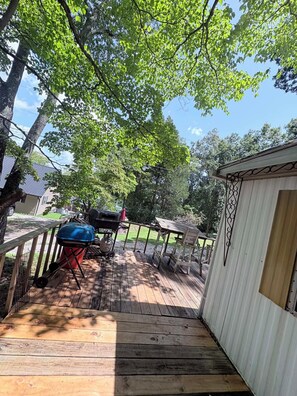 Eine Holzterrasse mit Grill, Gartenhaus und einem eingezäunten Rasenstück.