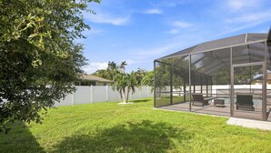 Un espacio al aire libre techado con piscina, mobiliario y césped.