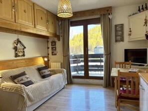 A cozy living room with a sofa, a dining table, and a TV. There is a large window with a view of trees and a mountain. - Ski-in/ski-out & foot of the slopes, 4th floor, balcony, tv, 30m², Les Orres (Les Orres)