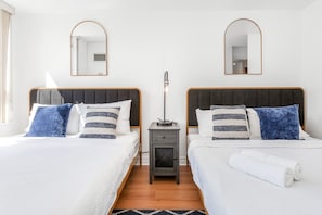 A hotel room with two beds, each with a headboard, a bedside table, a lamp, and a mirror on the wall. - City Retreat | 2BR 2BATH | Sleeps 8 | Free Parking (Mississauga)