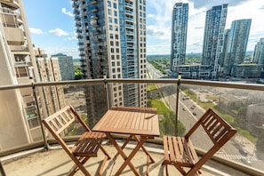 A balcony with a wooden table and two chairs, overlooking a cityscape with high-rise buildings. - City Retreat | 2BR 2BATH | Sleeps 8 | Free Parking (Mississauga)