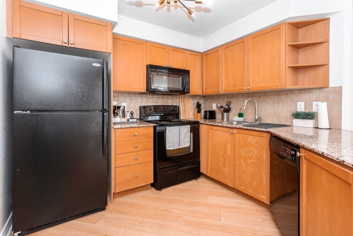 A kitchen with wooden cabinets, a black refrigerator, a microwave, a stove, and a dishwasher.