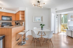 A modern kitchen with wooden cabinets, a stainless steel stove, and a dining area with a round table and white chairs. - City Retreat | 2BR 2BATH | Sleeps 8 | Free Parking (Mississauga)